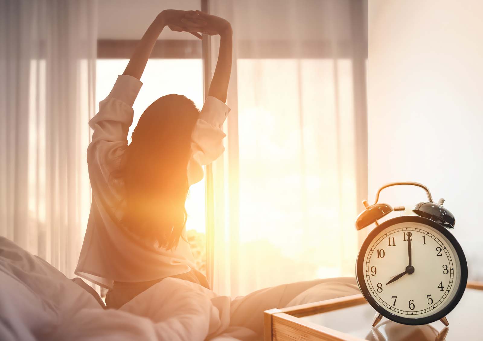 A woman wakes to a sunrise through her bedroom windows.