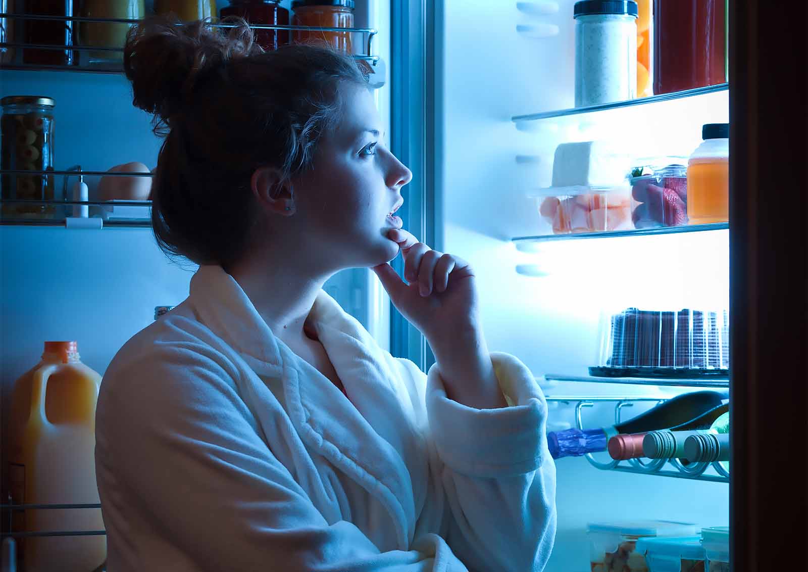 A young woman looks for a healthy late-night snack in the refrigerator.