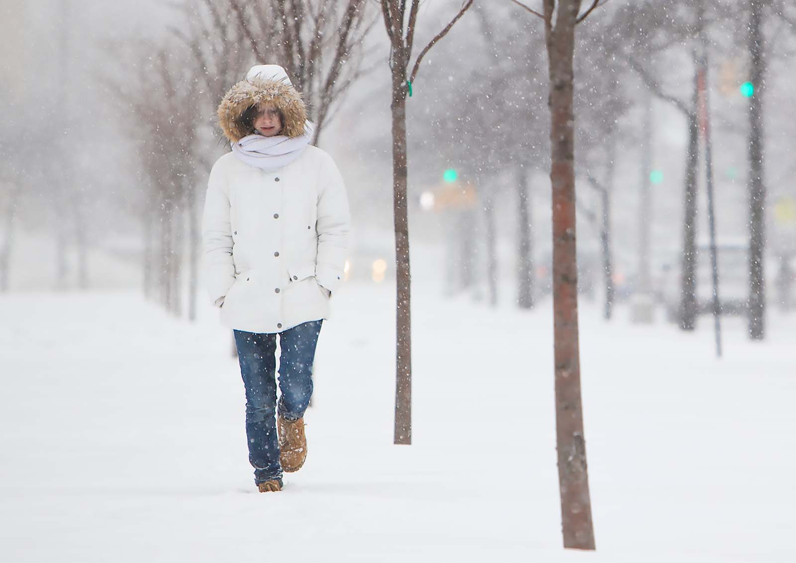 A woman walks alone on a city sidewalk in the snow.