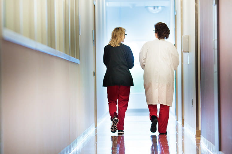 Two female hospital staff in conversation walking down a long hallway.