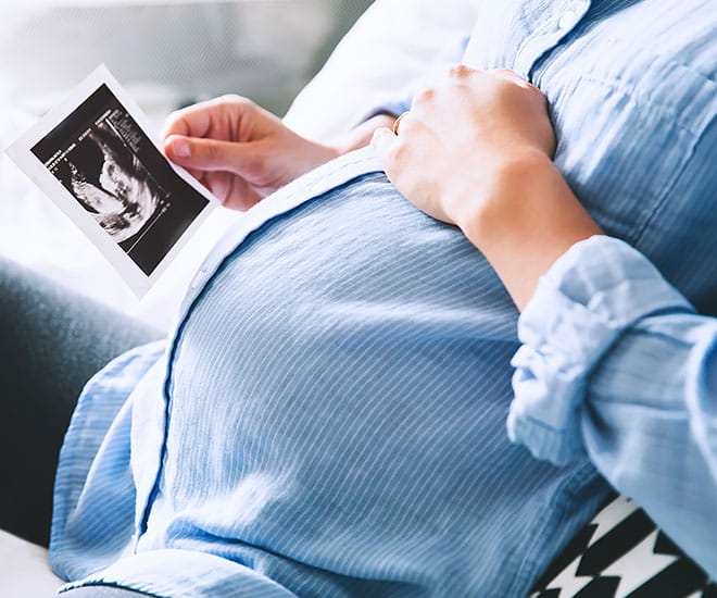 A seated pregnant woman looks at a sonogram of her soon to be born child.