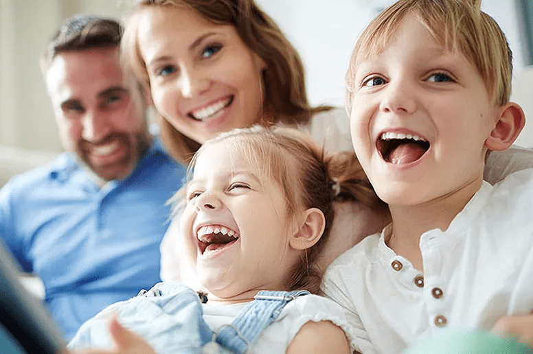 A family smiling and laughing on a couch while looking into camera