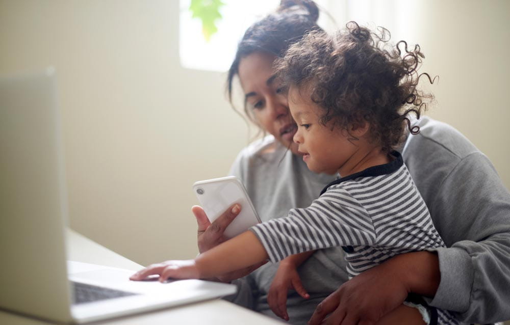 A woman works on her laptop while holding her baby