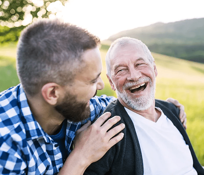 A senior sits outside, laughing with a younger man