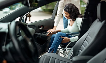 una mujer en silla de ruedas recibiendo asistencia para subir a un automóvil