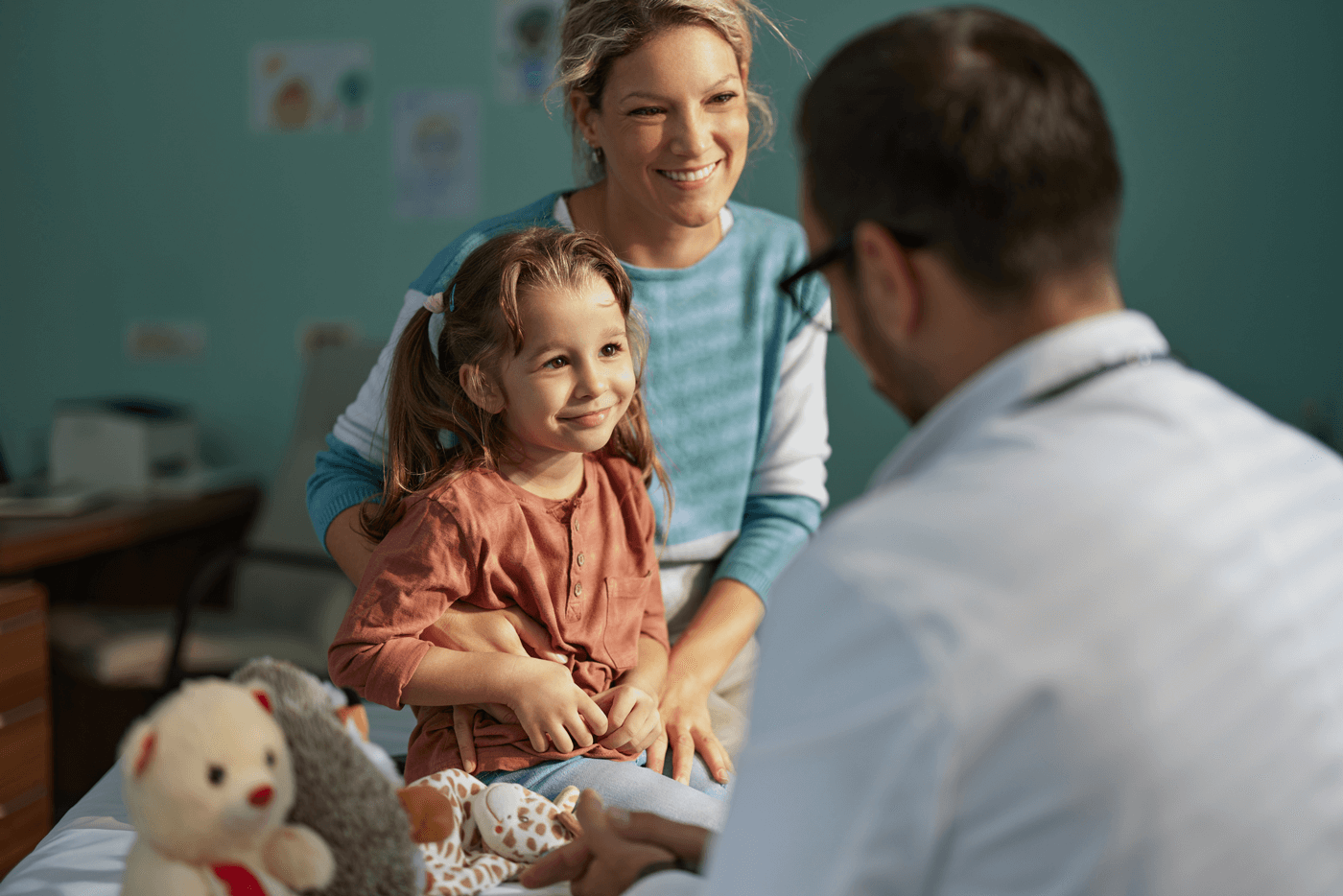 A young child sees a doctor in an exam room along with her mother
