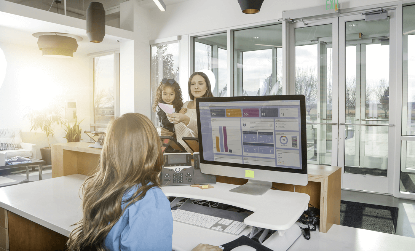 A woman talks with an employee at the front desk of a clinic