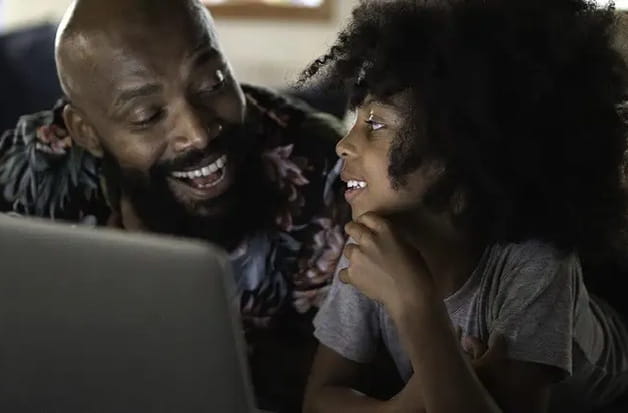 Un padre y un hijo se recuestan frente a una computadora portátil y chatean