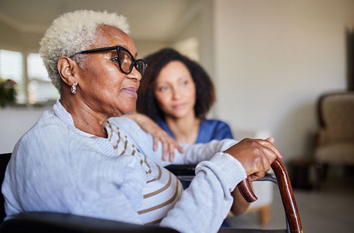 an older woman sits on a cough looking into the distance with a younger woman sitting next to her