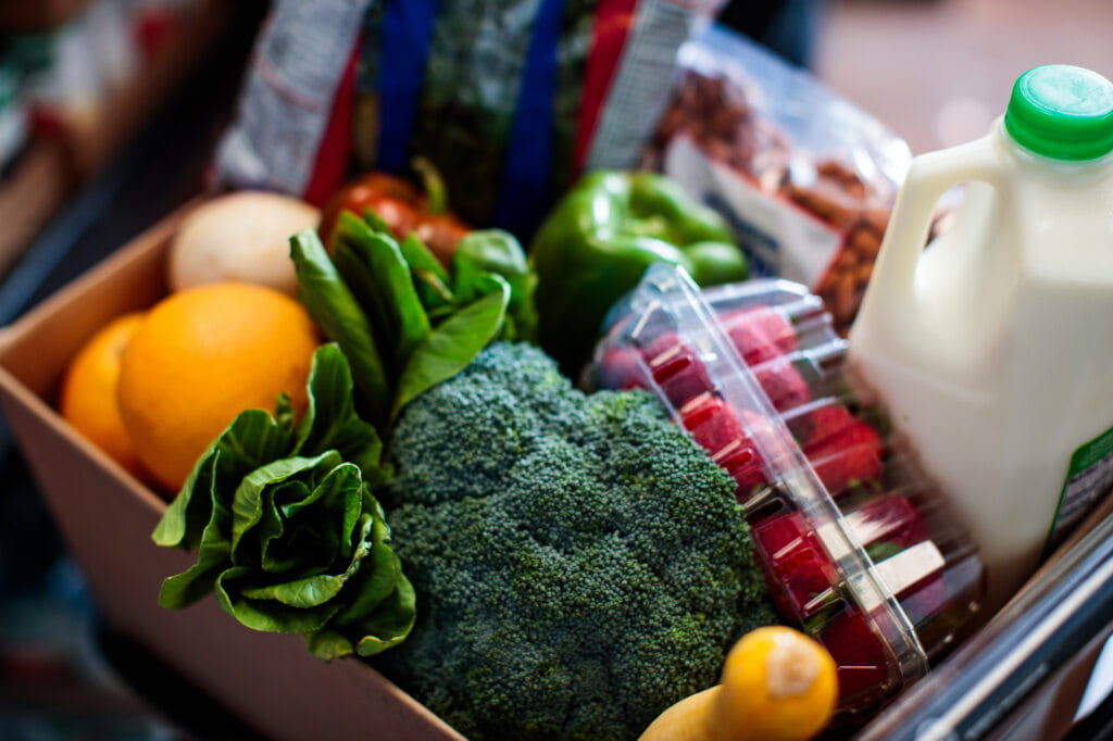Una caja de alimentos que incluye leche y diversas frutas y verduras