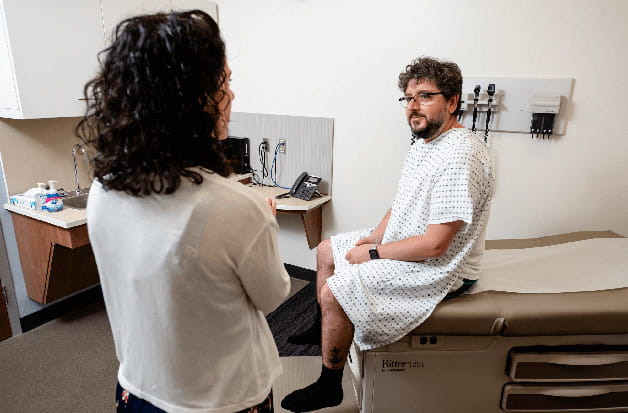 A man in a hospital gown sits on a table with a doctor