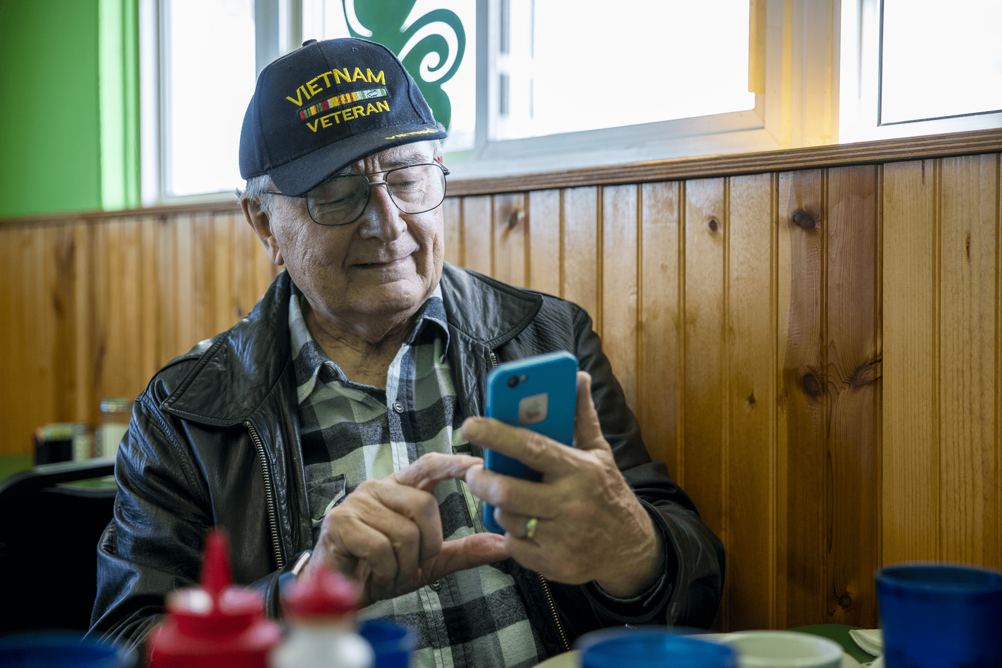 A senior sits at a table looking at his phone 