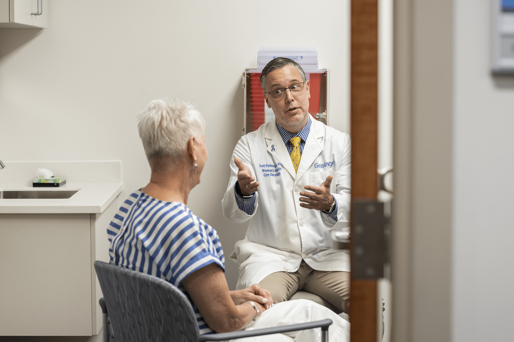 A doctor sits in a clinic room with a senior patient having a discussion