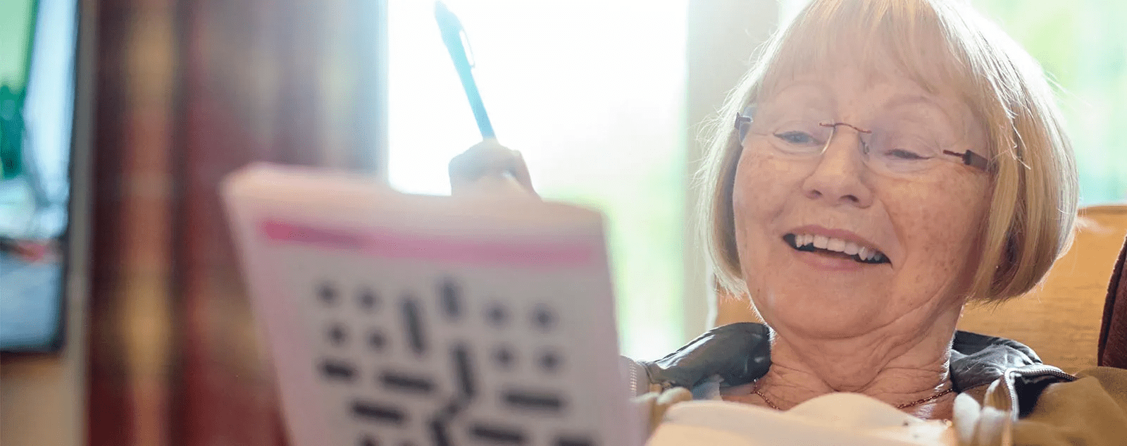 A senior woman in a chair works on a crossword puzzle