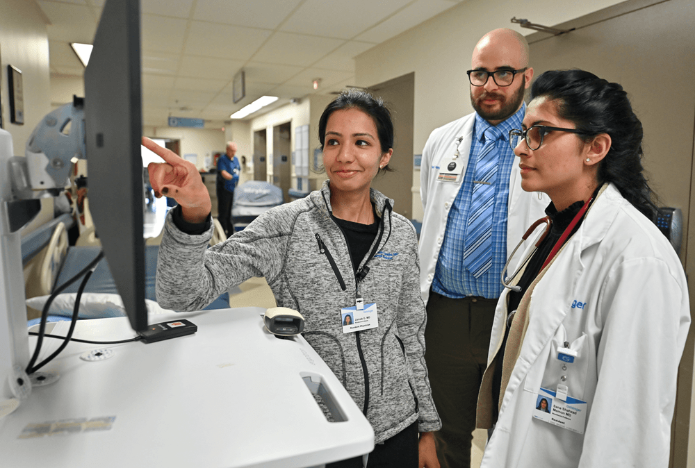 Un médico señala información en una pantalla de computadora y dos médicos miran