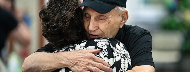An elderly man in a wheelchair high fives a younger woman