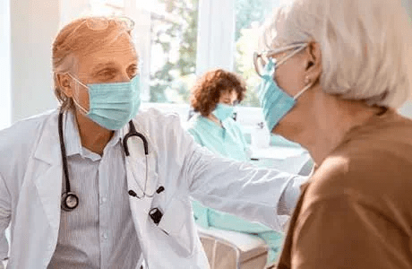 A doctor chats with a senior patient while holding her arm