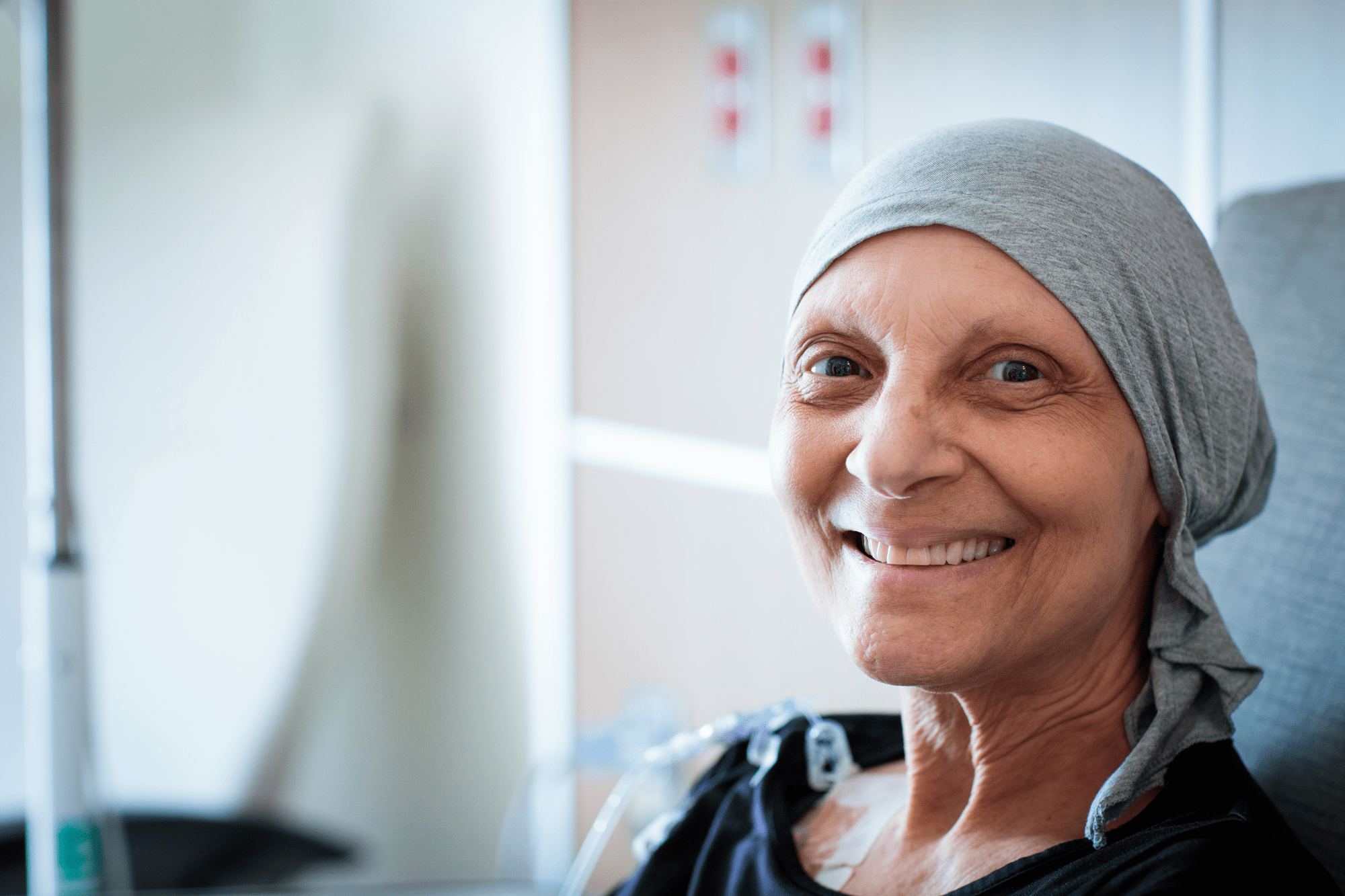 A senior patient in a hospital wearing a headwrap smiles into the camera