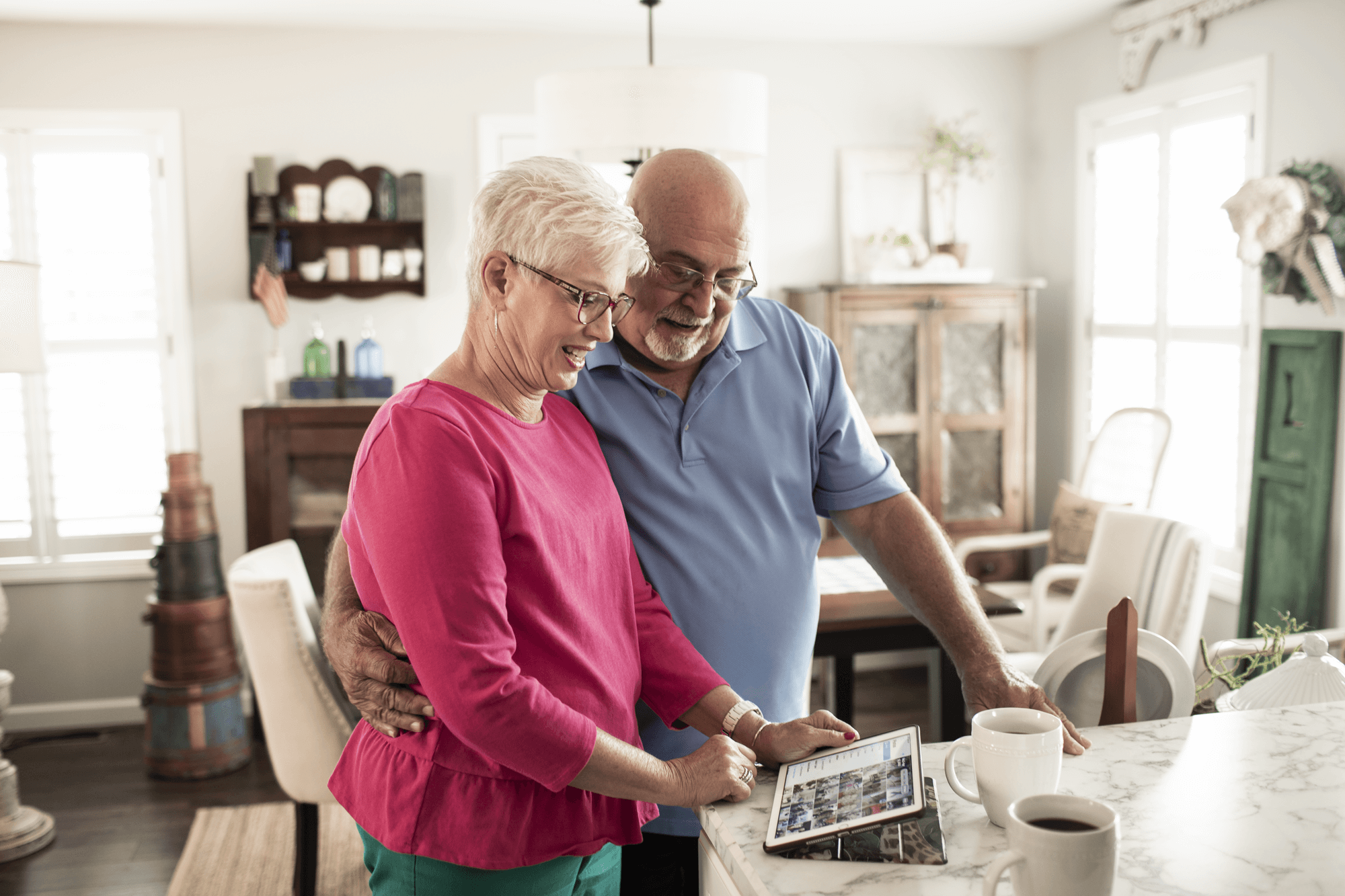 A senior couple stand at a home countertop looking at a tablet