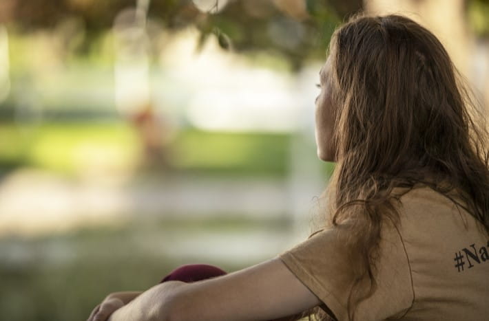 A young girl sitting on a lawn looking off into the distance