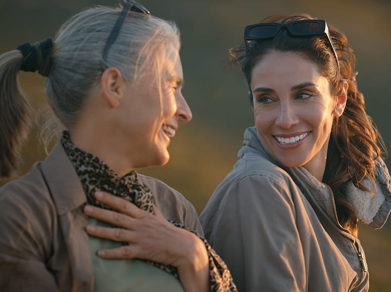 Adult daughter and mother sitting out doors smiling at each other