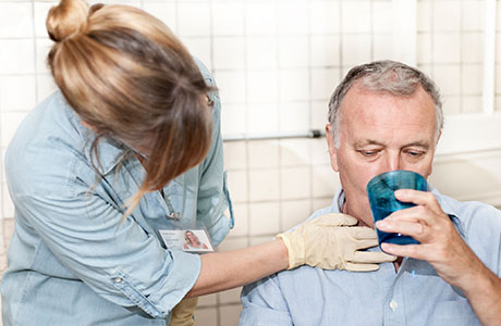 a female speech therapist giving an older male patient a glass of water