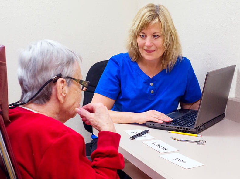 a female speech therapist at a laptop talking to an older patient