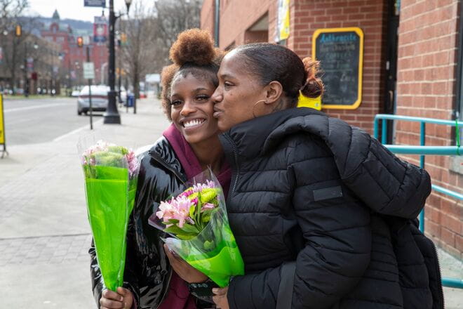 two woman standing outdoors holding flowers smiling