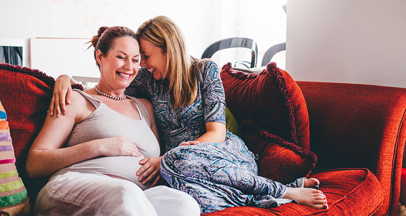 A pregnant woman smiling as another woman touches her stomach