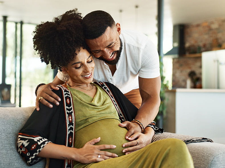 a pregnant woman and her partner holding her belly while smiling
