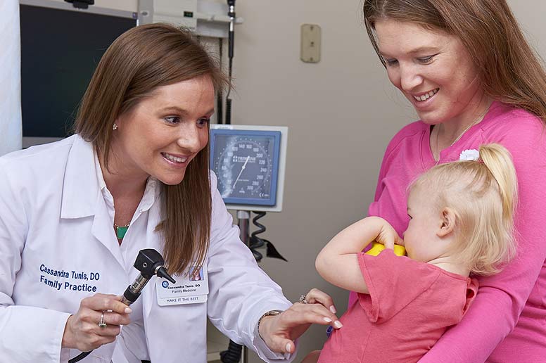 Mother holding daughter while smiling doctor starts the examination