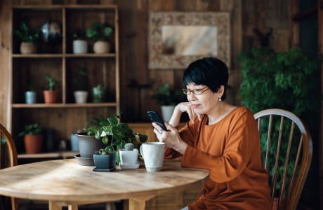 an older woman sits at a dining table looking at her cell phone
