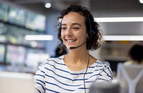 a young woman sits at her desk smiling with a headset on