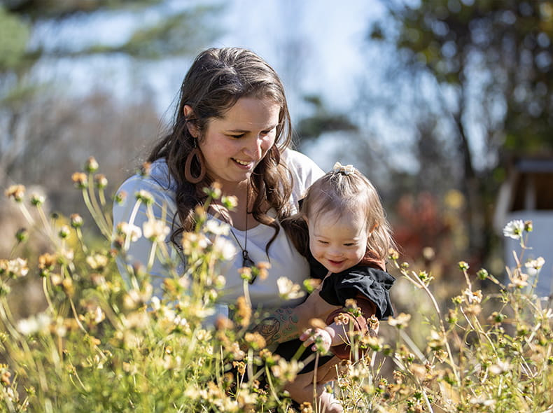 A mother holds her daughter in a field of flowers.