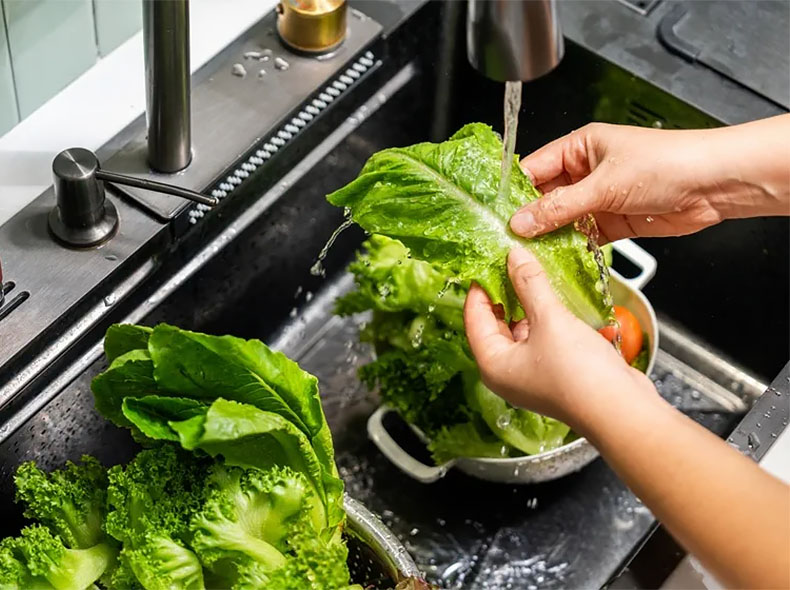 Fresh lettuce being washed under running water in a kitchen sink to promote food safety and help prevent foodborne illness.
