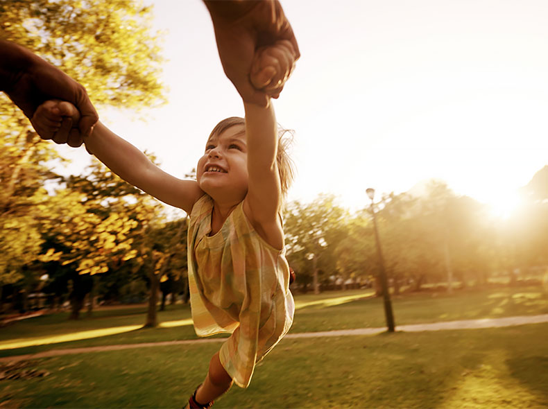 Child playing outdoors while being supported by adults, representing pediatric health and childhood wellness.