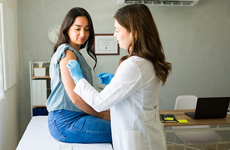 Young Hispanic woman is getting vaccinated by a professional medical worker.