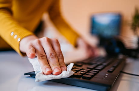 A person spring cleaning their office and keyboard with a paper towel.