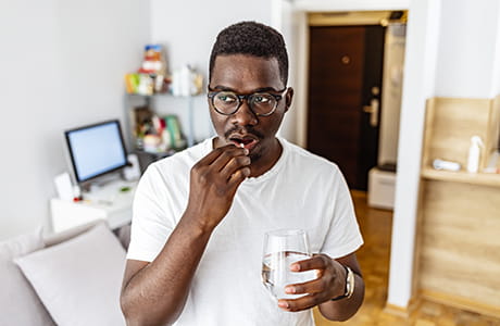 A man takes an OTC pain medication with a glass of water.