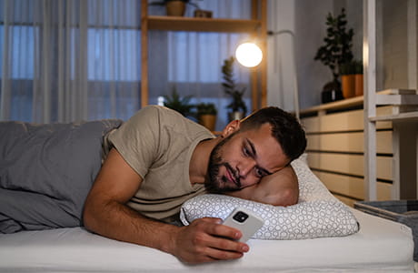 A sleepy man using a phone in the bed. 