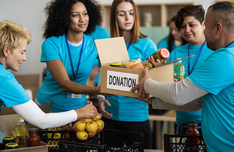 Women are placing putting food into a cardboard box for donation. 