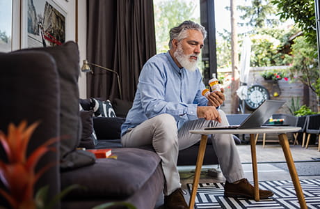 A man in his 50s is holding pill bottles while searching for information online