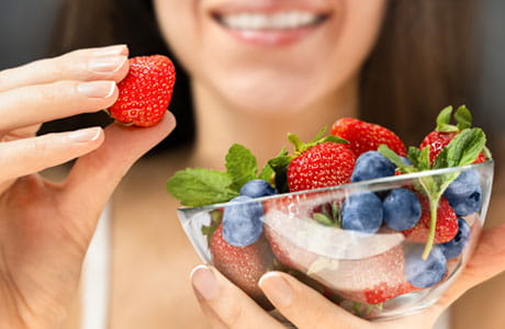 A woman smiling while eating a bowl of low-FODMAP berries