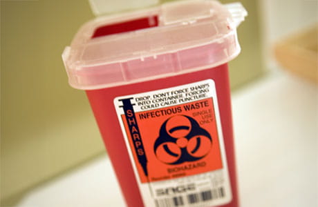 A plastic sharps container with 'biohazard infectious waste' labeling for getting rid of used needles
