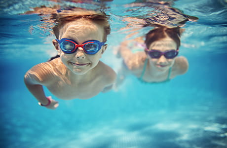 Smiling kids enjoying underwater swim in the pool.