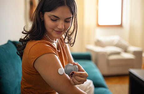 Young diabetic patient teenage woman using applicator to attach glucose sensor on arm.