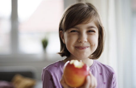 A female child smiling eating an apple.