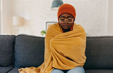 Young woman wearing a beanie with a blanket wrapped around her. 