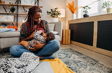 a mother sits on the floor in her living room breast feeding her baby