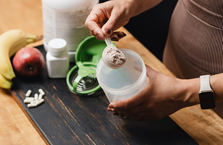 a woman stands at a counter scooping a powdered supplement